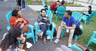 Group of young people seated in a circle of chairs outside.