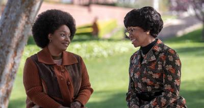 Christina Jackson as Barbara Lee and Regina King as Shirley Chisholm sit on a bench under a tree, talking. 