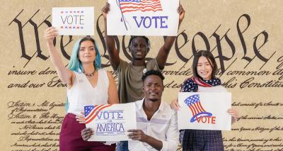 Four people of color holding signs that say "Vote" with enlargement of U.S. Constitution showing "We the People" in background.