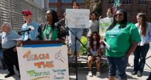 Black, Brown, and White participants and speaker at podium outside; sign on podium says "Teach the Truth"; sign held by participant says "Students deserve the truth Youth empowered in the struggle"