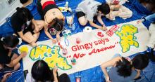 Students seated on the floor painting a large banner that says "Gingy says No Arena."