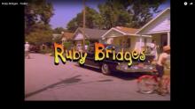 street scene from the movie Ruby Bridges showing a neighborhood with cars, people walking, and riding bikes